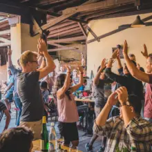 viele Menschen stehen im Weingut und heben die Hände in die Luft