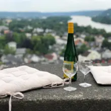 zwei Sitzkissen, zwei Weingläser und eine Flasche Wein auf einer Steinbank