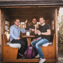 drei Männer sitzen mit Bier in einem kleinen Holzhäusschen