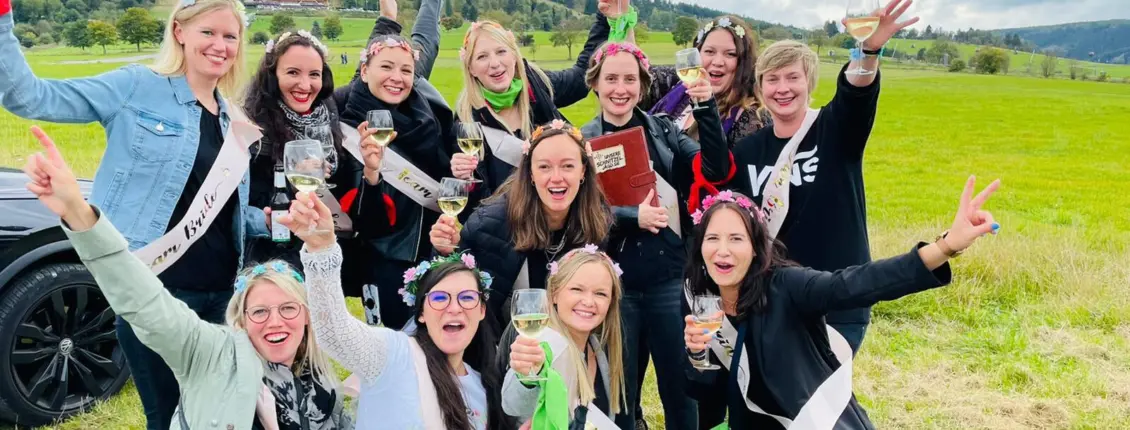 Gruppenfoto von Frauen auf einer Wiese. Alle heben ein Weinglas in die Luft.