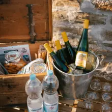 Tisch mit Snackkiste, Weingläsern, Weinflaschen und Wasser