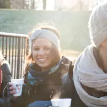 drei lachende Menschen mit Glühwein in der Hand und Mützen auf dem Kopf